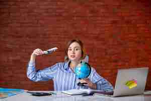 Free photo front view travel agent behind her working place holding little globe and toy plane map assistant agency world managers indoors operator service