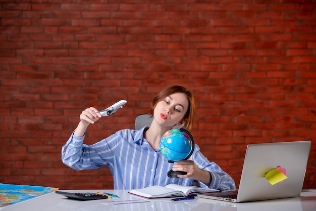 Free photo front view travel agent sitting behind her working place observing little globe map assistant agency world manager indoors service