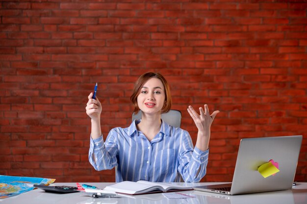 Front view travel agent sitting behind her working place with laptop and notepad indoors map agency world ticket global manager assistant