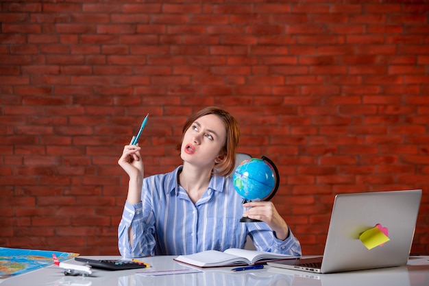 Free photo front view travel agent sitting behind her working place with little globe assistant agency map indoors service world manager