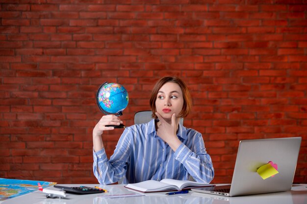 Front view travel agent sitting behind her working place with little globe assistant map indoors manager world operator agency service