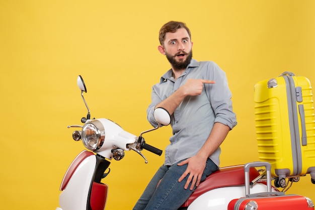 Free photo front view of travel concept with wondering young man sitting on motocycle with suitcases pointing back on it on yellow