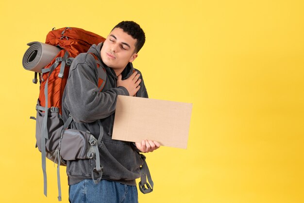 Front view traveler man with backpack holding cardboard putting hand on his chest