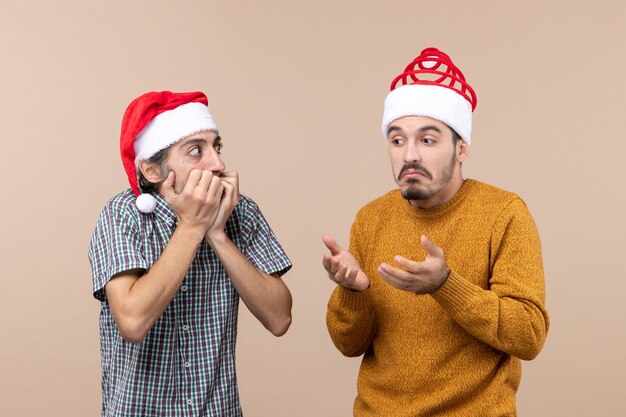 Front view two amazed guys with santa hats on beige isolated background