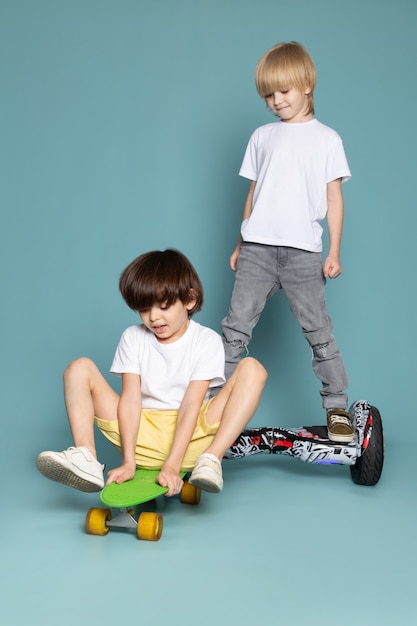 Free photo a front view two boys adorable sweet cute happy riding scooter and segway on the blue floor