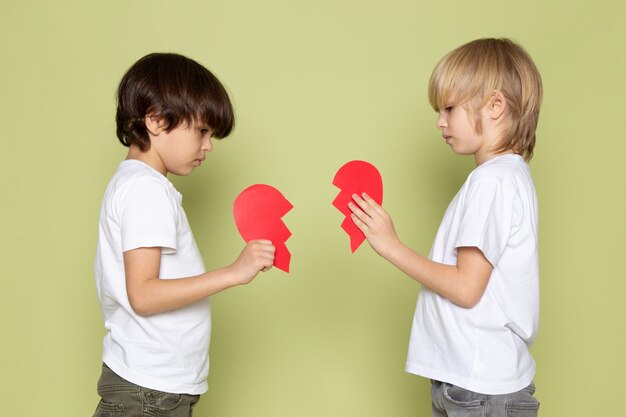 A front view two boys in white t-shirts holding red teared heart shape on the stone colored space