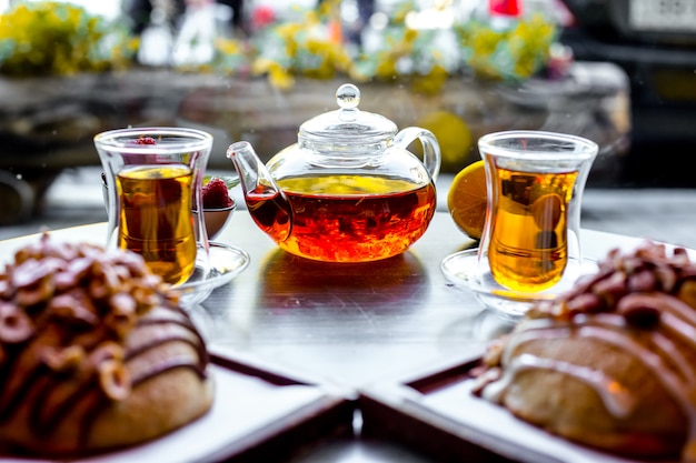 Front view two buns with nuts and two armouda glasses of tea with tea kettle on the table