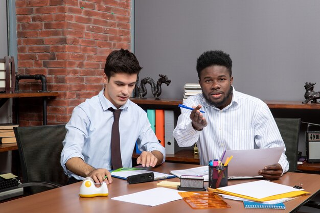 Front view two business partners working in office one of them pointing finger camera