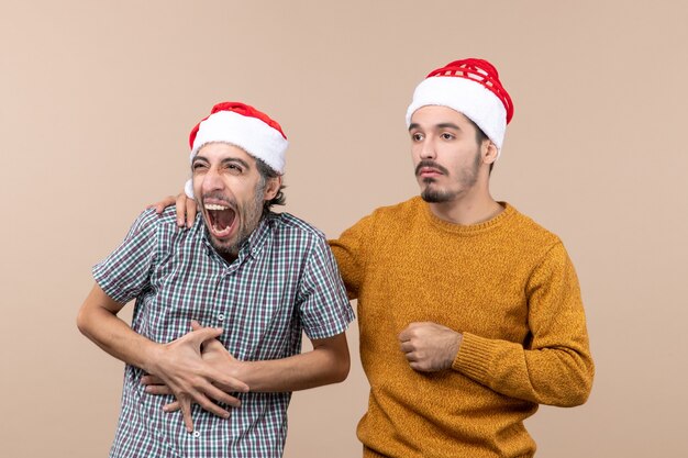 Front view two guys with santa hats sad one putting his hand on the others shoulder on beige isolated background