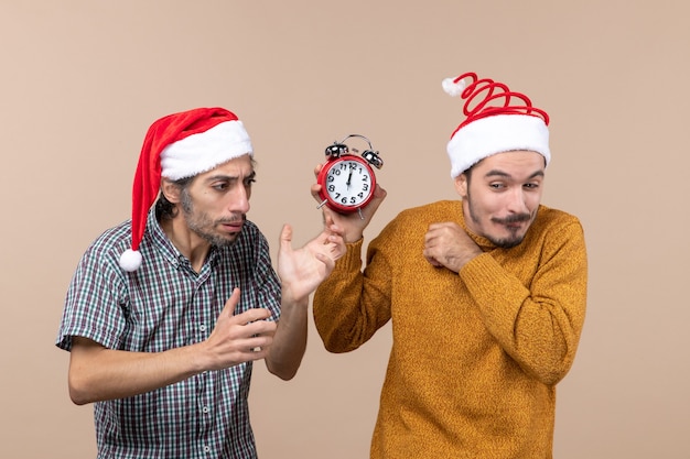 Front view two men one confusing and the other holding an alarm clock on beige isolated background