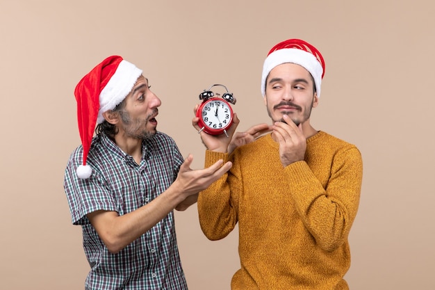 Front view two men one holding an alarm clock and the other saying something on beige isolated background