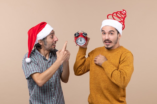 Front view two men one holding an alarm clock and the other telling something on beige isolated background