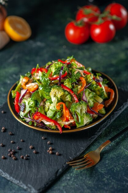 Front view of vegan salad with fresh ingredients in a plate and pepper on black cutting board