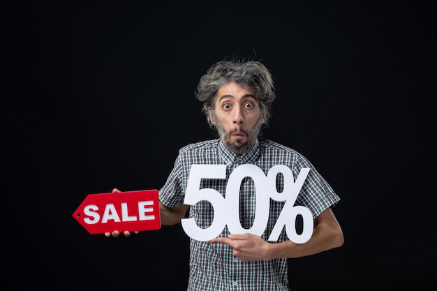 Free Photo front view of very confused man holding up mark and red sale sign on dark wall