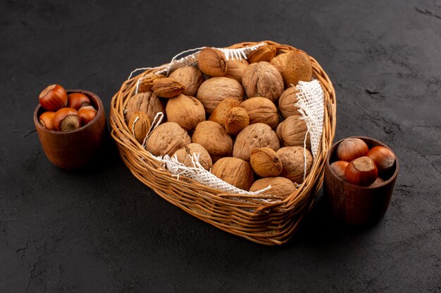 front view walnuts and hazelnuts inside basket and brown pots on the dark floor