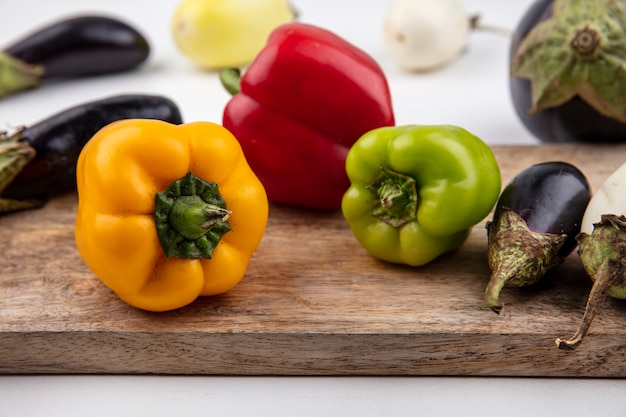 Front view white and black eggplant on a cutting board with colored peppers