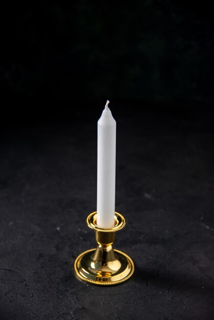 Front view of white candle in golden stand on black