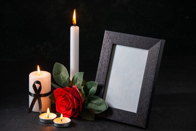 Front view white candle with picture frame and flower on dark surface