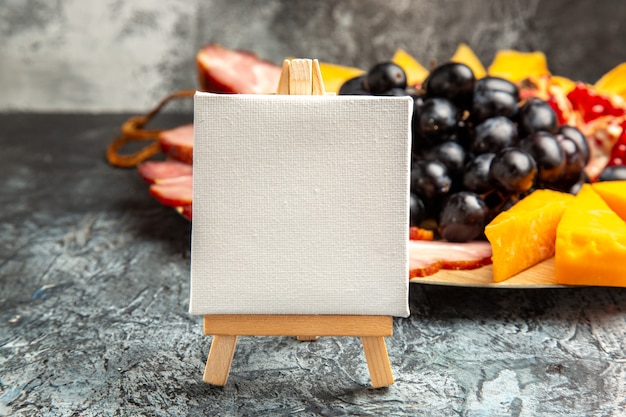 Free photo front view white canvas on wooden easel grapes meat slices on wood plate on dark