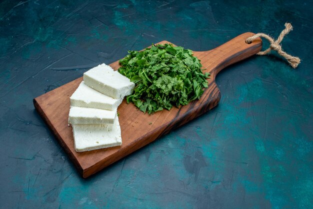 Front view white cheese with fresh greens on dark-blue background.