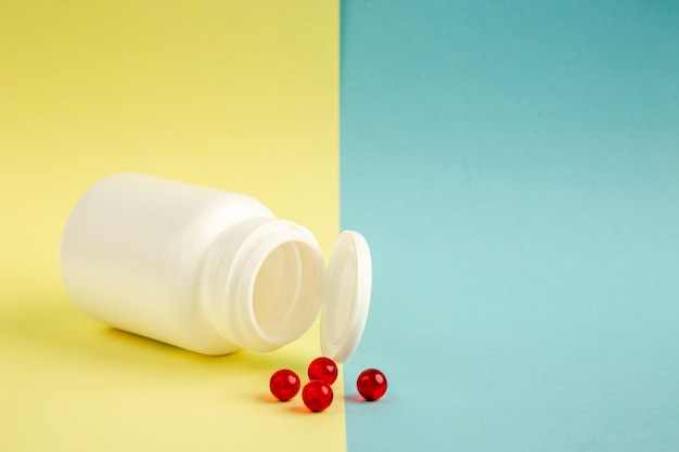 front view white plastic can with red pills on yellow-blue background