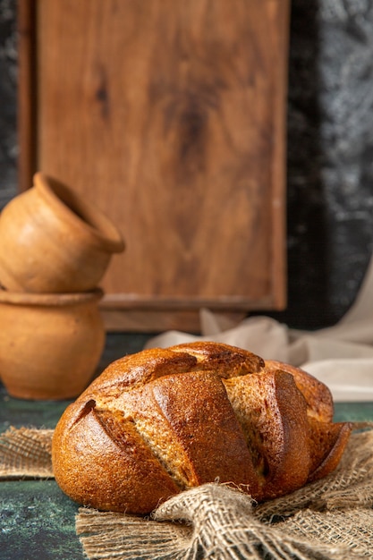 Front view of whole black bread on brown towel potteries on dark colors surface