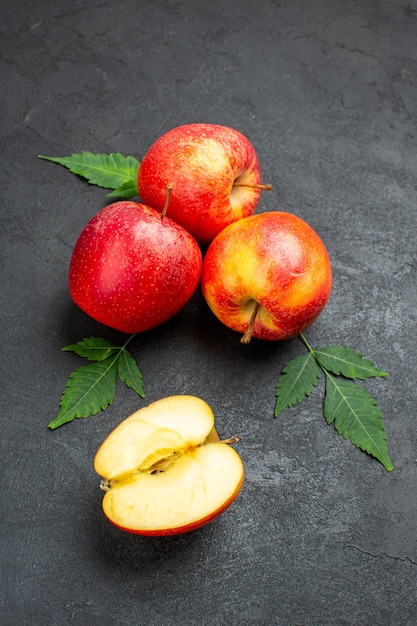 Front view of whole and cut fresh red apples and leaves on black background