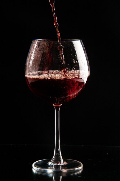 Front view wine glass getting poured with red wine on a black color drink champagne xmas alcohol