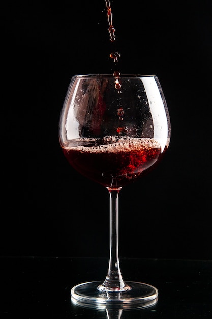 Front view wine glass getting poured with red wine on black color drink champagne xmas alcohol