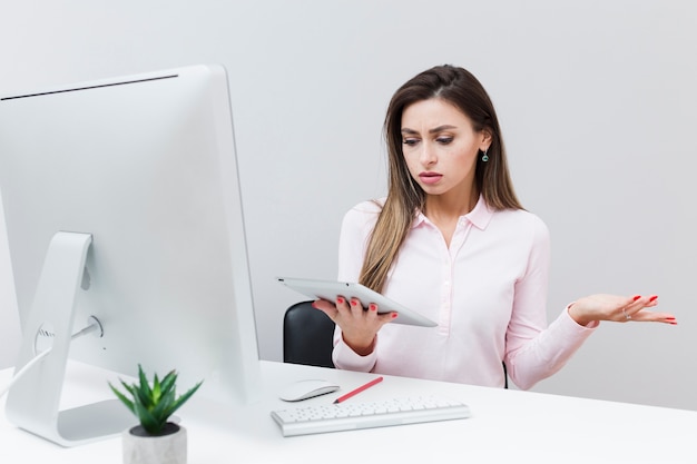 Front view of woman being frustrated with her tablet while sitting at desk