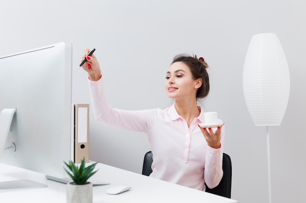 Front view of woman at desk holding cup of coffee