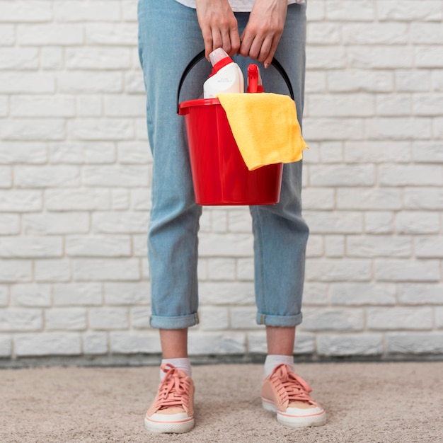 Front view of woman holding bucket with cleaning supplies