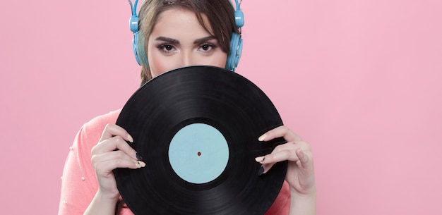 Front view of woman holding up vinyl record while wearing headphones