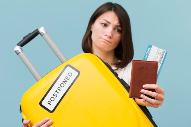 Free photo front view woman holding a yellow baggage with a postponed sign