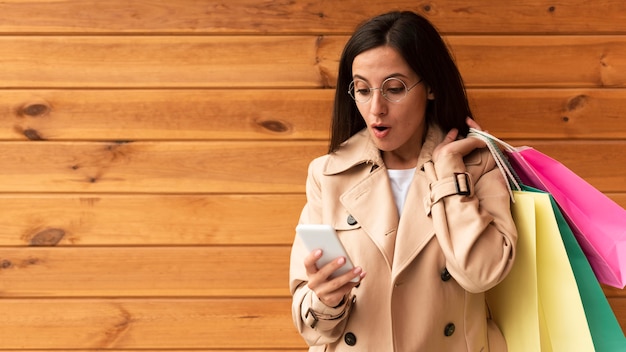 Free Photo front view of woman looking shocked at her phone while holding shopping bags