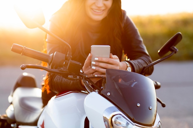 Front view of woman looking at smartphone while sitting on her motorcycle