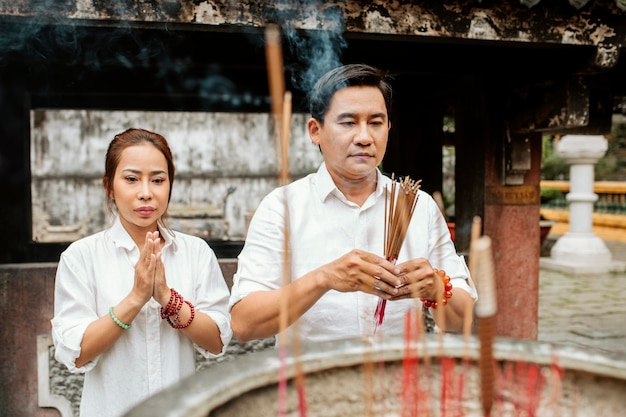 Front view of woman and man praying at the temple with burning incense