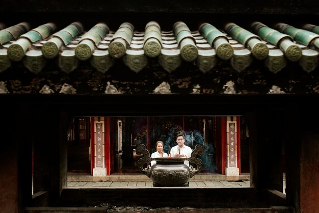 Front view of woman and man praying at the temple with burning incense