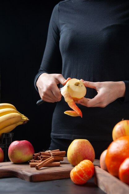 Front view woman peeling fresh apple with knife on kitchen table