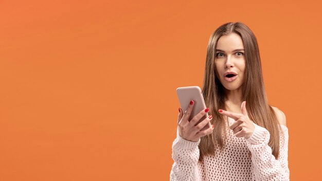 Front view of woman pointing at smartphone she's holding