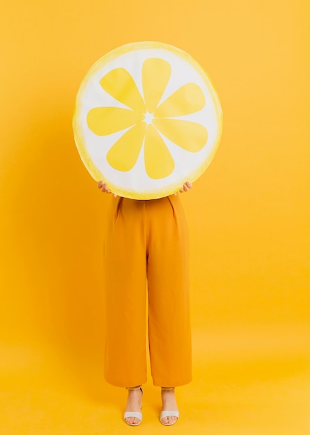 Front view of woman posing while covering head with lemon slice decoration