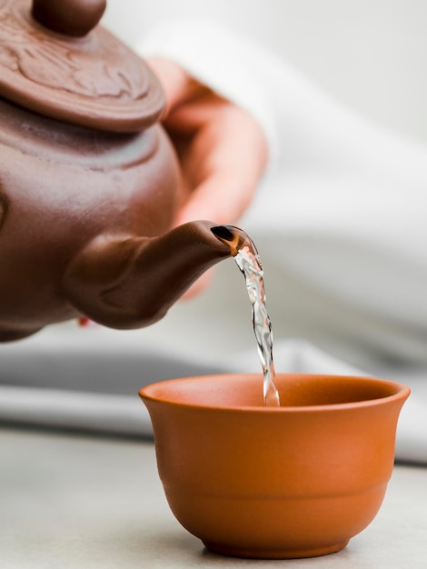 Front view woman pouring tea from clay teapot