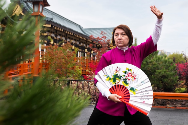 Free Photo front view woman practicing tai chi with fan