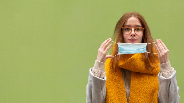 Front view of woman putting on medical mask with copy space