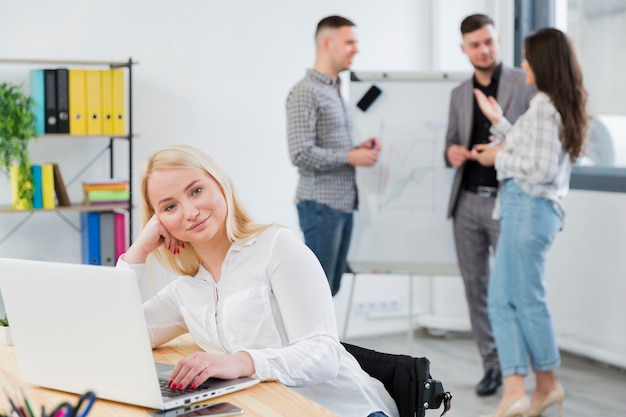 Free Photo front view of woman in wheelchair posing at work while colleagues converse