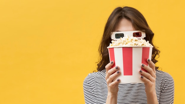 Front view woman with 3d glasses covering her face with a popcorn bucket