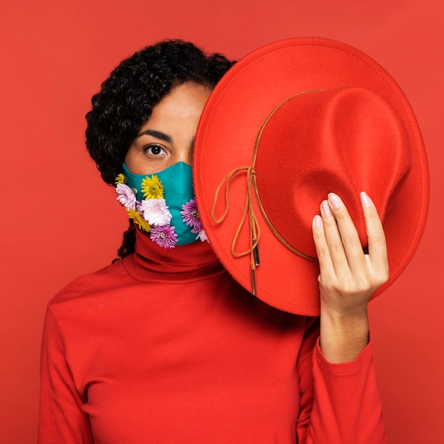 Free Photo front view of woman with flowers on her mask posing with hat