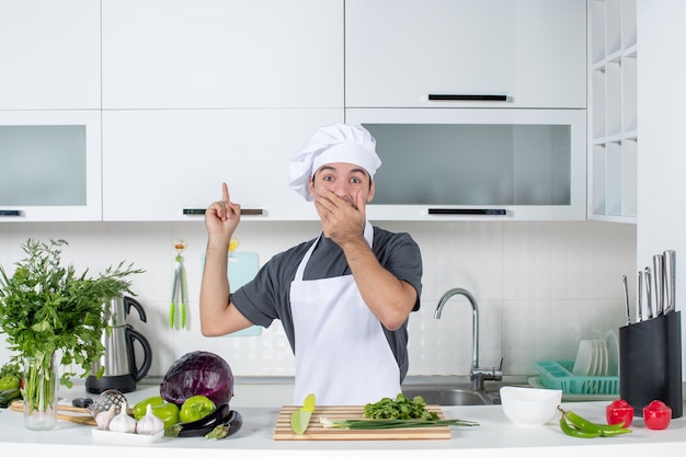 Front view wondered young cook in uniform pointing at cupboard