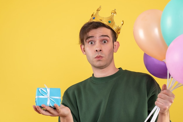 Front view wondered young man with crown holding balloons on yellow 