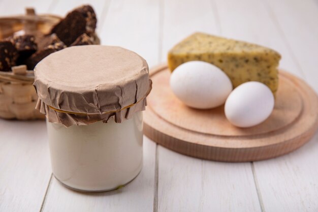 Front view yogurt in a jar with cheese and chicken eggs on a stand on a white background